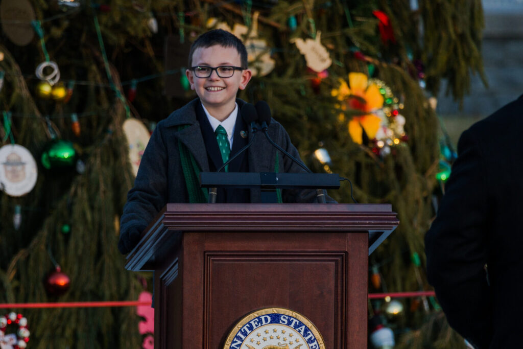 The People's Tree Essay winner stands beneath the tree at the Capitol